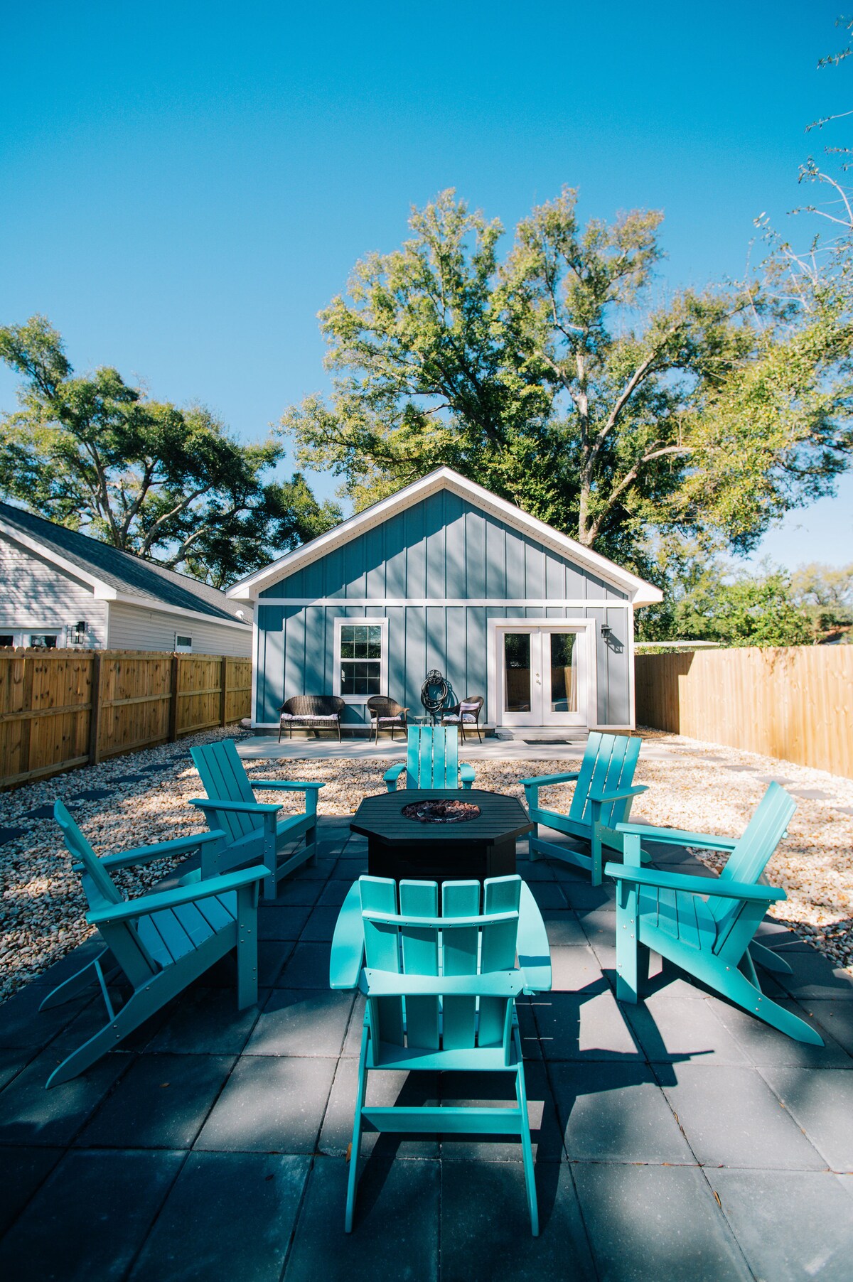 Fenced backyard with fire pit and Adirondack chairs at Auer House Pensacola